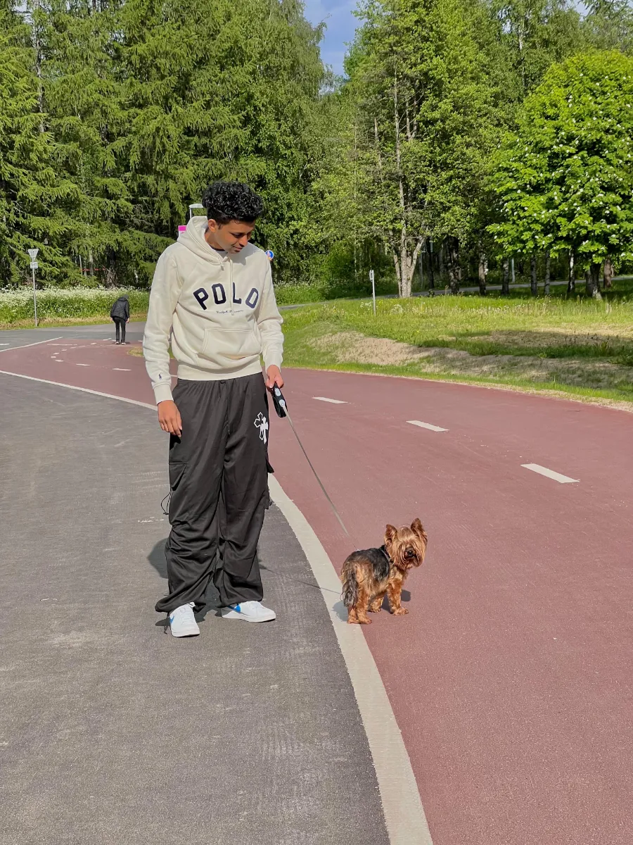 Kavindu Ravishan Perera walking a small dog along a red cycle path by the woods