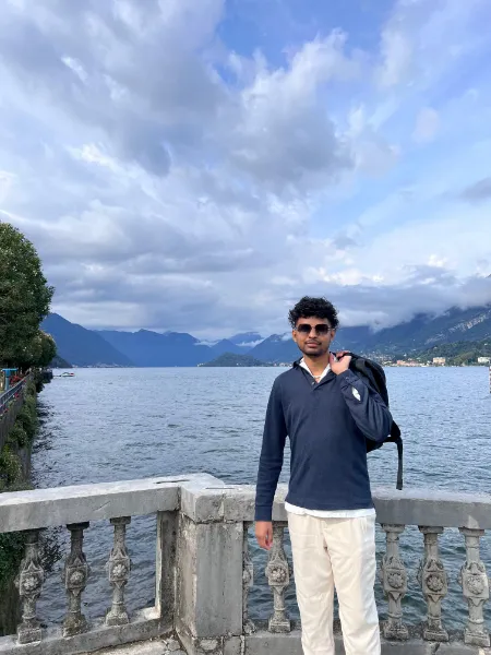Kavindu Ravishan Perera at a stone balustrade by a lake, clouds low over the mountains