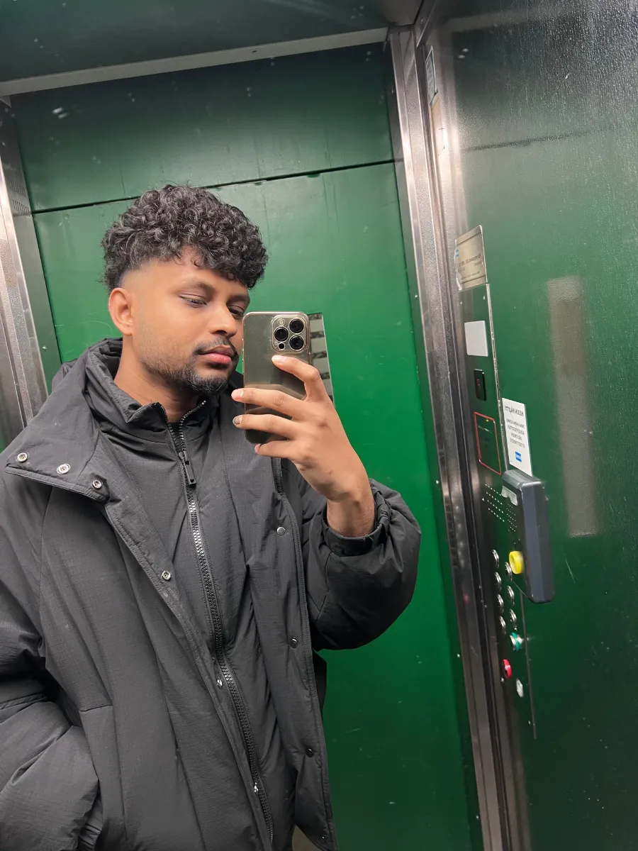 Kavindu Ravishan Perera in a black winter jacket, taking a mirror photo in a green lift