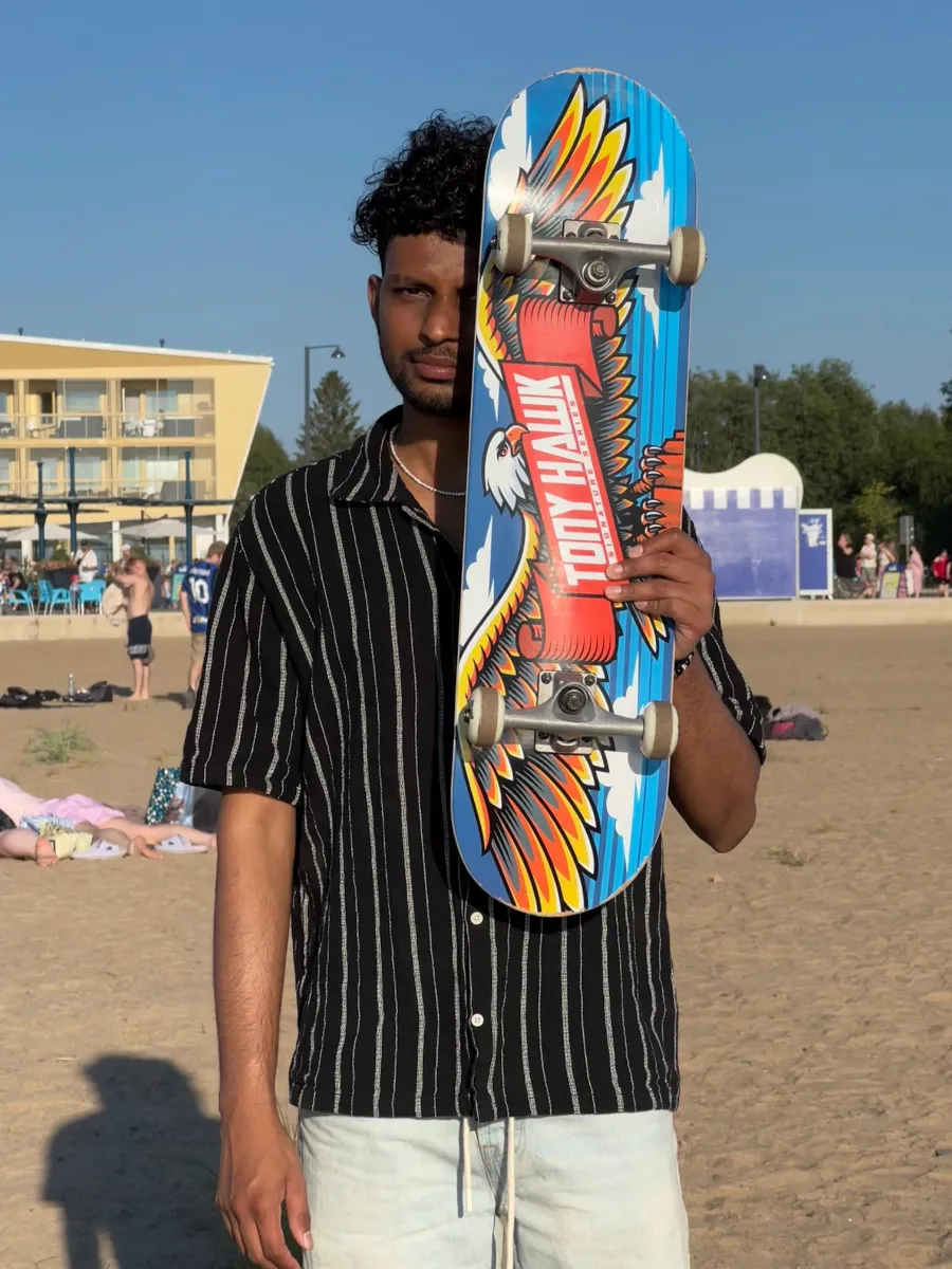 Kavindu Ravishan Perera on a sandy beach in summer, holding a skateboard over half his face